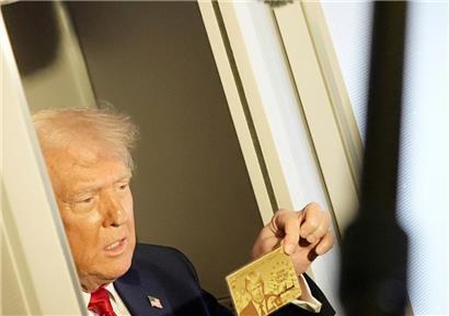 Präsident Donald Trump hält die goldene 5-Millionen-Dollar-Karte hoch, während er an Bord der Air Force One auf dem Weg nach Miami zu Reportern spricht
