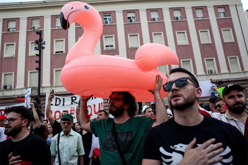 Protestplakate und pinke Flamingos bei abendlicher Demonstration in Tirana, Albanien