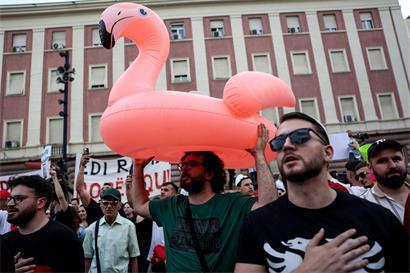 Protestplakate und pinke Flamingos bei abendlicher Demonstration in Tirana, Albanien