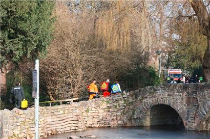 Rettungskräfte und Kriminaltechniker gehen in der Nähe des Tatortes eine kleine Brücke hinauf
