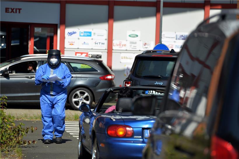 Rheinland-Pfalz, Bitburg: Eine ehrenamtliche Helferin des Deutschen Roten Kreuzes (DRK) im Schutzanzug verteilt Unterlagen an Urlaubsrückkehrer, die auf das Coronavirus getestet werden
