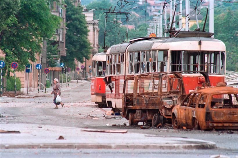 Sarajevo am 25. Juni 1992: Eine Frau überquert eine Straße in der einstigen Olympia-Stadt. Ausgebrannte und zerstörte Fahrzeuge auf den Straßen dienten als Schutz vor den serbischen Scharfschützen, die von den umliegenden Bergen aus die Zivilbevölkerung terrorisierten.

