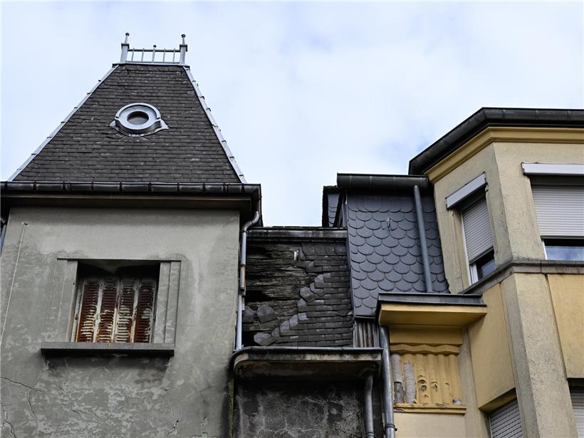 Beschädigtes Dach mit Feuchtigkeitsschäden, die sich auf das angrenzende Nachbarhaus ausbreiten, sichtbare Wasserschäden