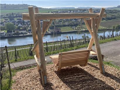 Kind schaukelt auf Holzschaukel mit grüner Landschaft und weitem Ausblick bei klarem Himmel