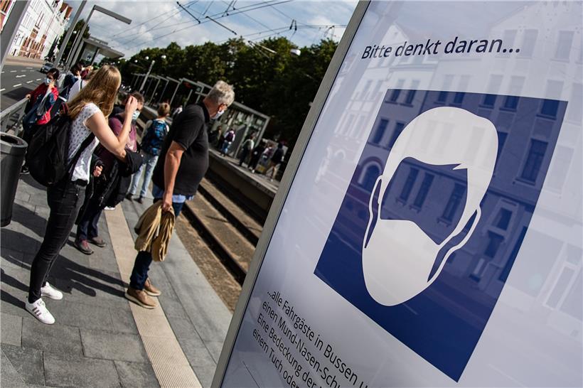  Schüler stehen neben einem Plakat, das auf eine Maskenpflicht in Bussen und Bahnen hinweist.
