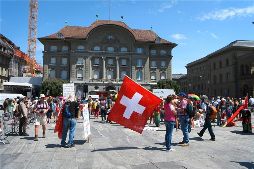 Schweiz, Bern: Eine Frau nimmt mit einer großen Schweizerfahne an einer Demonstration gegen Corona-Maßnahmen auf dem Bundesplatz teil. Eine Gegendemonstration findet auch statt.
