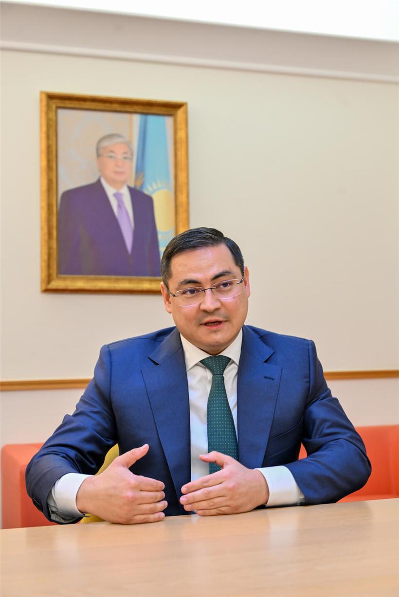 Shukhrat Ibragimov steht vor einem Foto von Kasachstans Präsident Qassym-Schomart Toqajew in offizieller Umgebung