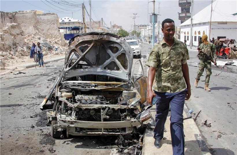 Sicherheitskräfte und Zivilisten gehen an einem Fahrzeugwrack in Mogadischu vorbei. Zuvor explodierte eine Autobombe an einem Checkpoint nahe dem Präsidentenpalast.
