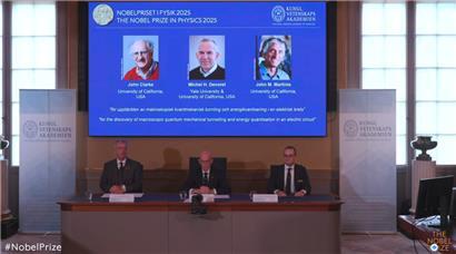 Standbild aus dem Livestream zur Bekanntgabe des Nobelpreises für Physik 2025: Auf einer Leinwand ist die Präsentation der diesjährigen Preisträger, die in den USA forschenden Quantenphysiker John Clarke (l-r), Michel Devoret und John Martinis, zu sehen
