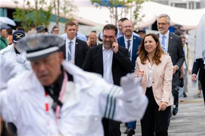 Stéphanie Obertin beim Rundgang über die Weltausstellung in Begleitung von Daniel Sahr, dem Direktor des Luxemburger Pavillon. Im Vordergrund ein Sicherheitsbeamter, der den VIP-Gästen den Weg freimacht.
