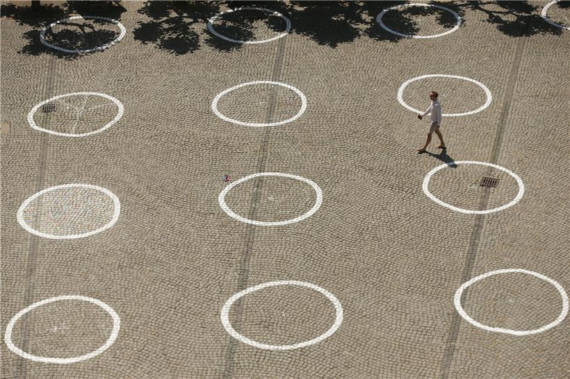 Symbolträchtiges Foto: Im deutschen Düsseldorf geht ein Mann über einen Platz, auf den Kreise zur Regelung von Menschenansammlungen gemalt wurden
