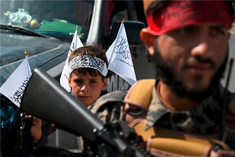 Taliban-Fahnen in der Hand, Taliban-Stirnband am Kopf: Ein Junge steht in Kabul hinter einem Kämpfer der neuen Herrscher über Afghanistan

