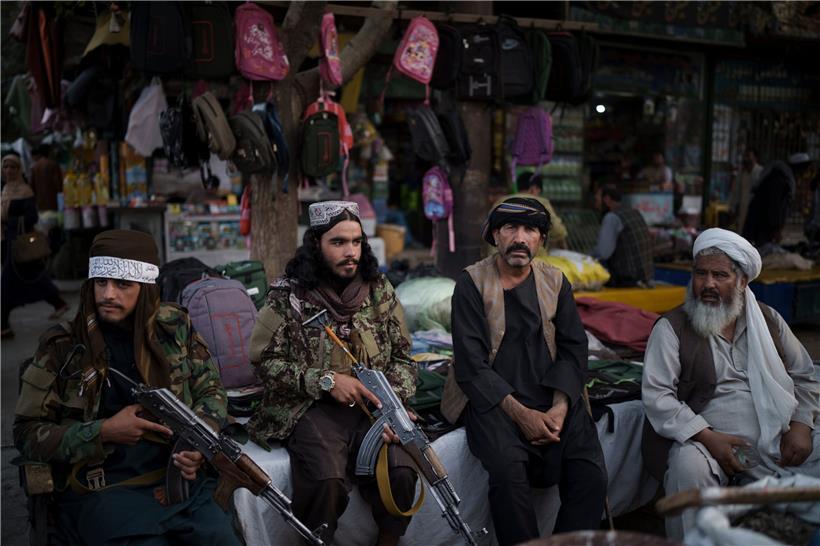 Taliban-Kämpfer sitzen in der afghanischen Hauptstadt Kabul neben Straßenverkäufern auf einem lokalen Markt und halten dabei Waffen in den Händen
