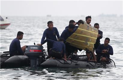 Taucher der indonesischen Marine ziehen ein Flugzeugteil aus dem Wasser in ein Boot
