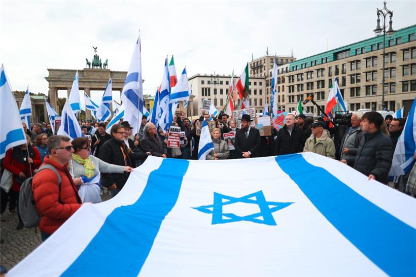 Teilnehmer einer proisraelischen Demonstration in Berlin halten gemeinsam eine große israelische Flagge. Die Demonstration „Gemeinsam gegen das Verbrechen der Hamas an Israelis und Palästinensern“ findet anlässlich des ersten Jahrestages des Überfalls der Hamas auf Israel vor dem Brandenburger Tor statt.
