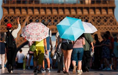 Touristen mit Regenschirmen, um sich während einer Hitzewelle in der Nähe des Eiffelturms in Paris vor der Sonne zu schützen
