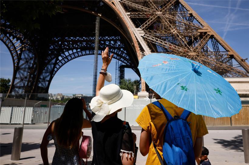 Touristen schützen sich mit Schirmen und Hüten vor der Sonne am Eiffelturm in Paris
