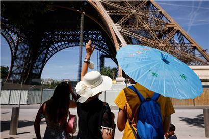 Touristen schützen sich mit Schirmen und Hüten vor der Sonne am Eiffelturm in Paris
