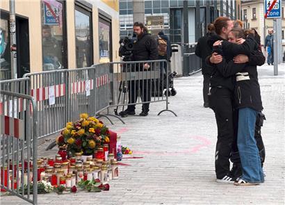 Trauernde Personen stehen am Tatort des Messerangriffs
