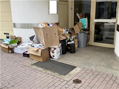 Papier und Karton stapeln sich trotz blauer Recyclingtonnen vor Hauseingängen, Müllentsorgung und Recyclingprobleme sichtbar
