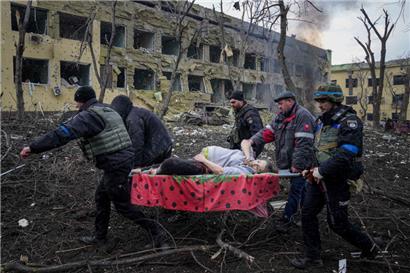 Ukrainische Rettungskräfte und Freiwillige tragen eine verletzte schwangere Frau aus einer Entbindungsklinik, die durch russischen Beschuss in Mariupol zerstört wurde
