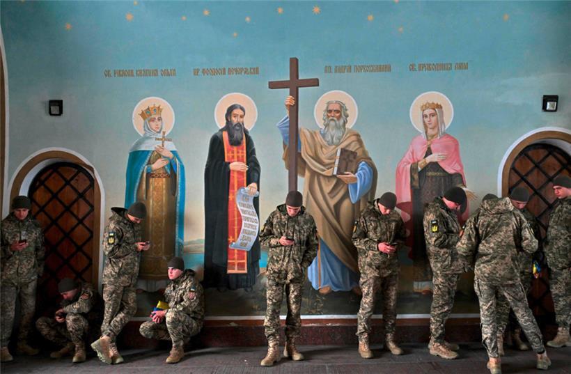 Ukrainische Soldaten blicken auf ihre Smartphones, während sie inmitten der russischen Invasion in der Ukraine am 1. November 2023 neben den Fresken in der St. Michaels-Kathedrale in Kiew stehen und sich vor dem Herbstregen schützen.
