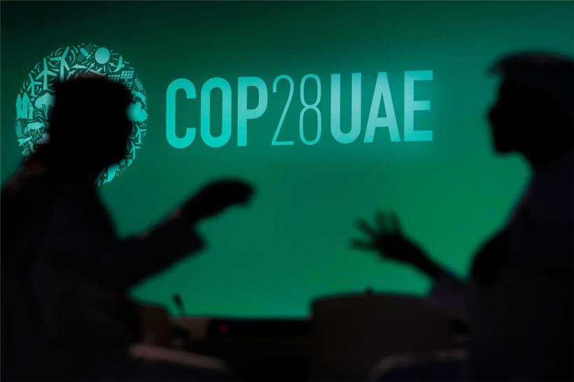 Vereinigte Arabische Emirate, Dubai: Zwei Menschen unterhalten sich vor einem Logo des UN-Klimagipfels COP28. Bei dem COP28-Treffen wollen mehr als 190 Länder ab Donnerstag am Persischen Golf die erste große Bestandsaufnahme der Umsetzung der Pariser Klimakonferenz 2015 erstellen.
