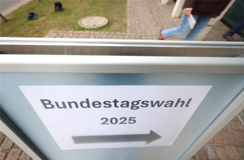 Wähler betreten hinter einem Hinweisschild mit der Aufschrift „Bundestagswahl 2025“ ein Wahllokal
