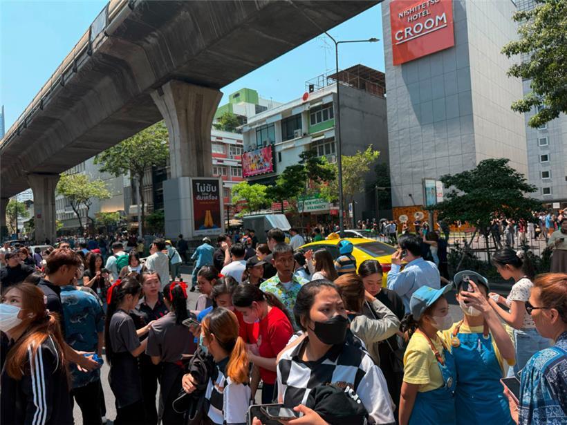 Wegen einem Erdbeben haben Menschen in Bangkok ihre Häuser verlasssen und stehen im Zentrum der Stadt auf einer Straße
