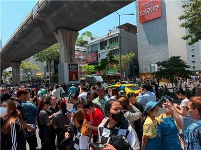 Wegen einem Erdbeben haben Menschen in Bangkok ihre Häuser verlasssen und stehen im Zentrum der Stadt auf einer Straße

