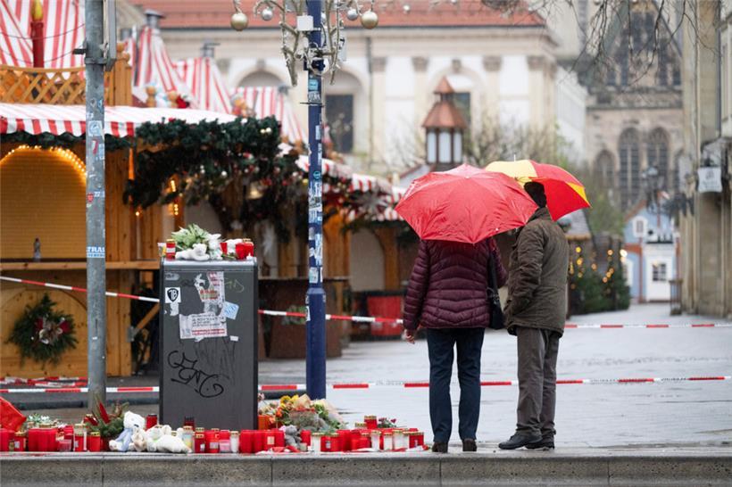 Zwei Passanten mit Regenschirmen stehen vor dem Weihnachtsmarkt
