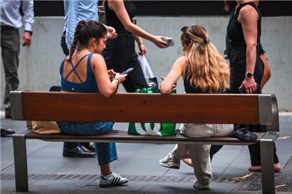 Zwei junge Frauen sitzen mit ihren Smartphones im Zentrum von Sydney. Australiens Premierminister Anthony Albanese räumte ein, dass es eine „schwierige Aufgabe“ sein werde, das vorgeschlagene Social-Media-Verbot umzusetzen.
