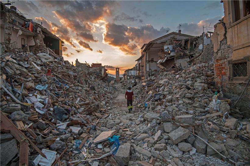 Zwischen eingestürzten Häusern in der italienischen Stadt Amatrice läuft ein Feuerwehrmann einsam dem wolkenverhangenen Himmel entgegen: Es ist eines der vielen Bilder, die fünf Jahre nach der Erdbeben-Katastrophe in Mittelitalien wieder hochkommen
