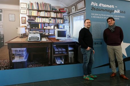 Die beiden Initiatoren der Ausstellung „Pir Kremer – ZesummegePIKtes“ und des Spektakels „Um Staminee“, Kulturhaus-Direktor Claude Mangen (l.) und Pascal Seil, Konservator beim CNL, vor einer Tafel, auf der man einen Blick ins Arbeitszimmer des facettenreichen Autors werfen kann