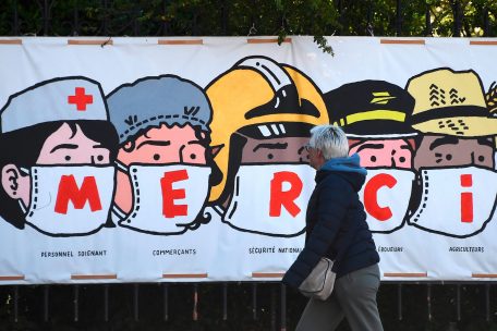 In Frankreich geht eine Frau an einem Banner vorbei, das jenen dankt, die in dieser Krise arbeiten müssen