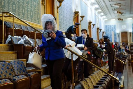 Menschen suchen Schutz auf der Tribüne des Repräsentantenhauses, während Demonstranten versuchen, in die Repräsentantenkammer im US-Kapitol einzudringen. Einige Personen haben sicherheitshalber Gasmasken angezogen oder halten diese bereit.