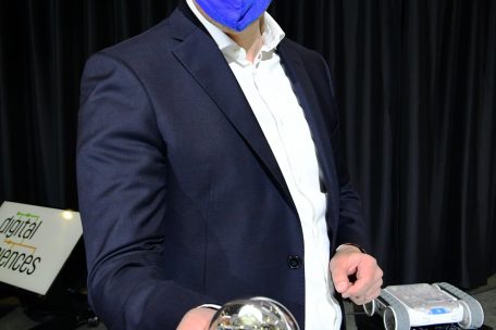 Claude Meisch hält einen kleinen Roboter, der in einer durchsichtigen Kugel integriert ist, in die Kamera unseres Fotografen