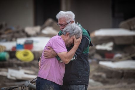 Weinend liegen sich zwei Brüder vor ihrem von der Flut zerstörten Elternhaus in den Armen