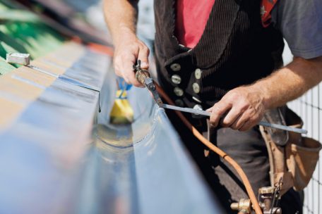 Ein Bauklempner lötet ein Fallrohr: In Luxemburg herrscht ein Handwerkermangel<br />