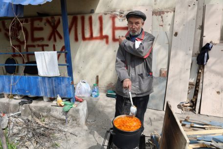 Ein einheimischer Zivilist kocht neben seinem Haus in Mariupol, einem Gebiet unter der Regierung der Volksrepublik Donezk in der Ostukraine, mit einem Schild mit der Aufschrift „Bombenschutz, Kinder“