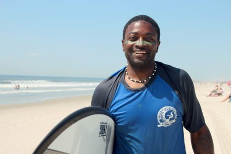 Lou Harris, der Kindern Surfunterricht gibt, steht am Strand.
