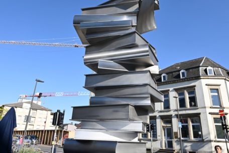 Im Auftrag der Gemeinde Petingen hat die Künstlerin Florence Hoffmann mit mehreren Partnern im Team eine monumentale Säulen-Skulptur in Form überdimensionaler, unregelmäßig aufgeschichteter Bücher aus rostfreiem Stahl geschaffen
