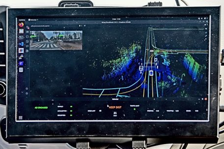 Das Display im Auto zeigt das dem System bekannte Kartenwerk (mit der „Schiene“ in der Straßenmitte) sowie die durch die Sensoren dynamisch erkannten Elemente. Besonders wichtig sind natürlich die anderen Verkehrsteilnehmer (die hier als weiße Gitterboxen erscheinen).