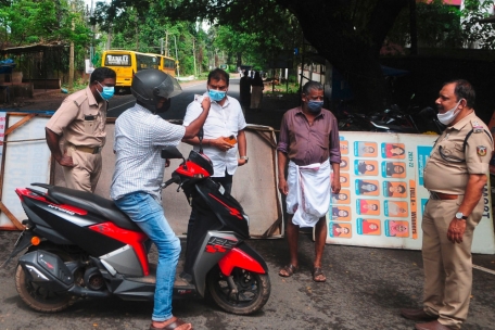 Polizei und Gesundheitsbeamte überprüfen den Ausweis eines Mannes an einem Kontrollpunkt entlang einer Straße, die in eine Sperrzone führt.