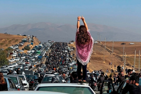 Dieses UGC-Bild, das Berichten zufolge am 26. Oktober 2022 auf Twitter gepostet wurde, zeigt eine unverschleierte Frau, die auf einem Fahrzeug steht, während sich Tausende auf den Weg zum Aichi-Friedhof in Saqez, Mahsa Aminis Heimatstadt, machen